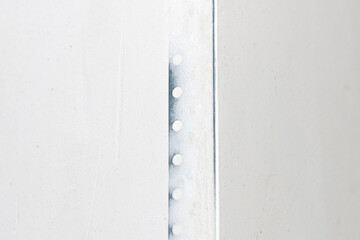Perforated metal profile corner to protect the plaster from cracking. The outer corner of the white drywall wall of the room. Unfinished repairs.