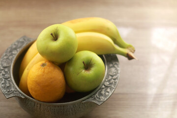 Antique bowl with bananas, apples and lemons on wooden table. Selective focus.