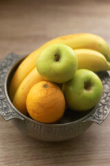 Antique bowl with bananas, apples and lemons on wooden table. Selective focus.