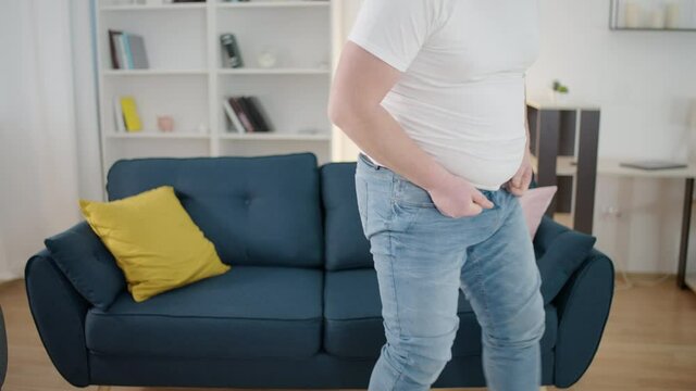 Annoyed obese man trying to button tight trousers at home, plus size problem