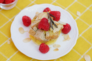 Homemade sweet bread pudding dessert with honey and raspberries in white dish on yellow table blackground.
