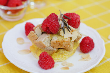 Homemade sweet bread pudding dessert with honey and raspberries in white dish on yellow table blackground.