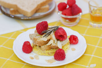 Homemade sweet bread pudding dessert with honey and raspberries in white dish on yellow table blackground.