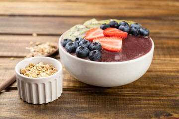 Brazilian typical acai bowl with kiwi, blueberry, granola and strawberry over wooden table