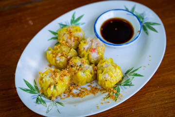 Chinese steamed dumpling with sauce in white dish on wooden table blackground.