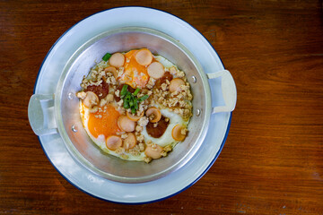 Thai food Pan Fried Egg with toppings   , sausage, minced pork in pan on wooden table blackground.