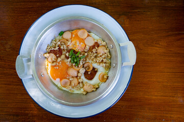 Thai food Pan Fried Egg with toppings   , sausage, minced pork in pan on wooden table blackground.