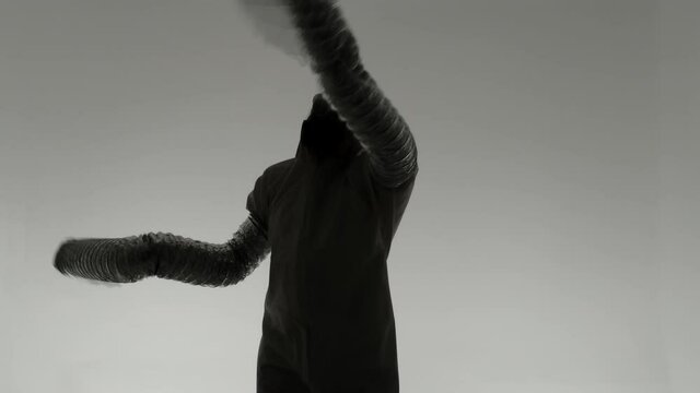 Strange silhouette of man in chemical protection suite with very long sleeves looking like monster hands dancing in front of white wall. Slow motion