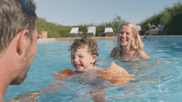 Parents teaching young son to swim on summer vacation in outdoor swimming pool using inflatable armbands - shot in slow motion