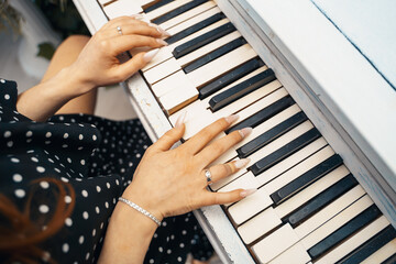 Female hands lie on the keys of a white piano