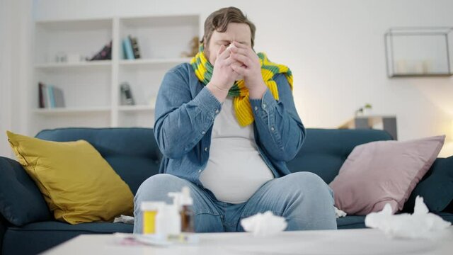 Overweight man in scarf drinking hot tea at home, feeling cold, symptom of fever