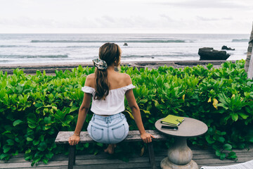 Unrecognizable tranquil female traveler resting on bench near ocean