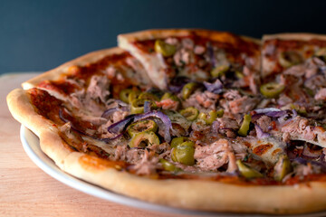 Freshky baked, homemade pizza al tonno, sliced on a white plate with dark background. Olives, tuna, onion, tomatoes.