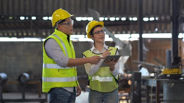 asian industrial Engineer manager man wearing eyeglass and helmet   discussion with mechanic worker woman while using digital tablet checking industry manufacturing large factory . inspection