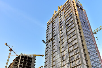 Tower cranes in action at construction site on blue sky background. A crane the conctruct the high-rise building. New residential skyscraper. Tall house renovation project, government programs