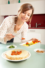 Young blonde caucasian woman smiling and preparing a pesto cheesecake in a kitchen.