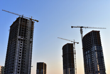 Fototapeta na wymiar Tower cranes in action at construction site on blue sky background. A crane the conctruct the high-rise building. New residential skyscraper. Tall house renovation project, government programs