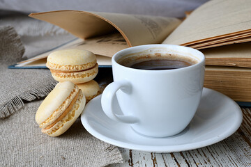 Сup of coffee, makroons and a book on the table.