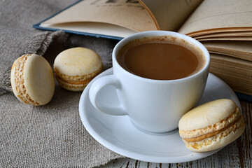 Сup of coffee, makroons and a book on the table.