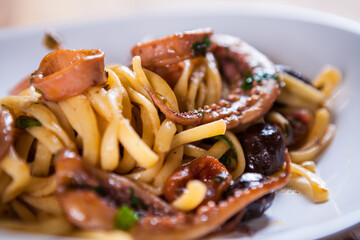 Pasta with calamari seasoned with red cherry olives and basil. Calamari spaghetti on white plate. Mediterranean pasta. seafood. Italian food. Fine dish. Fres food