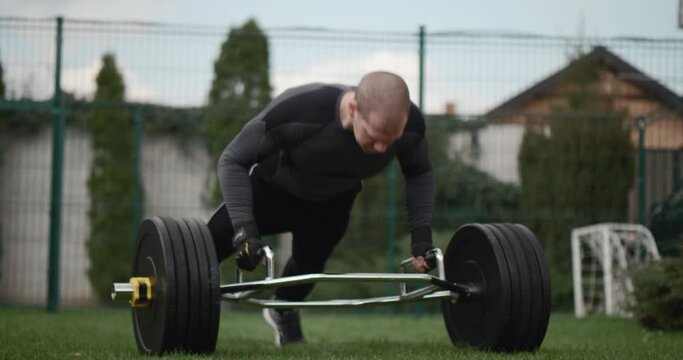 Muscular Fit  Young Man is Doing Push Up Exercises. He is Doing a Workout in in the yard on the green grass. Man uses a hex trap bar 
