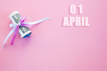 calendar date on pink background with rolled up dollar bills pinned by pink and blue ribbon with copy space.  April 1 is the first day of the month