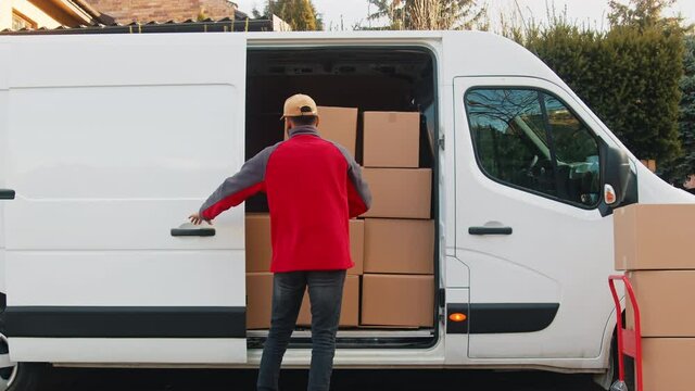 Young delivery man putting parcel into the van. Delivery during covid outbreak. High quality 4k footage