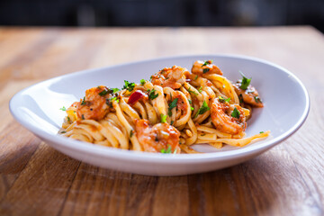 Spaghetti with shrimps, parsley and tomato sauce. Shrimps pasta on white plate. Seafood pasta on the wooden table in the kitchen. mediterranean  pasta. home made food