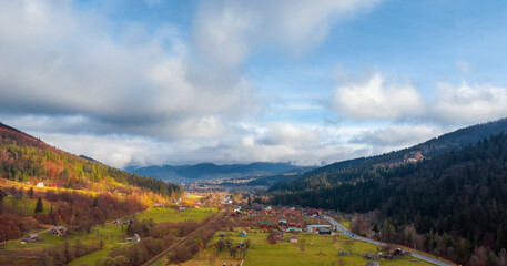 Fototapeta premium Aerial view of rural village between mountain hills covered with pine forest.