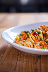 Spaghetti with shrimps, parsley and tomato sauce. Shrimps pasta on white plate. Seafood pasta on the wooden table in the kitchen. mediterranean  pasta. home made food