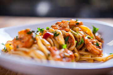 Spaghetti with shrimps, parsley and tomato sauce. Shrimps pasta on white plate. Seafood pasta on the wooden table in the kitchen. mediterranean  pasta. home made food