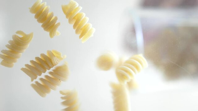 Macaroni of fusilli are falling on the glass, close up, food and ingredients, 4k