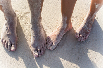 feet of a couple full of sand on the beach. 
feet in the sand
