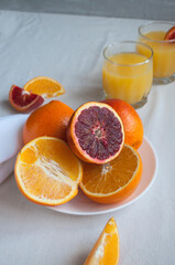 Sweet and juicy blood oranges and oranges, whole and cut on a white plate and gkasses of fresh orange juice. Fresh orange juice with Sliced oranges.