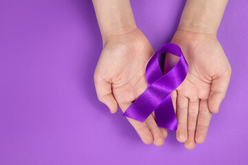 Purple day. World epilepsy day. Hands holding purple ribbon on purple background