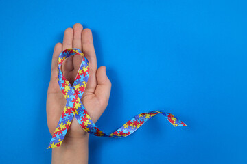 World Autism awareness day. Autistic boy hand holding puzzle pattern ribbon on blue background