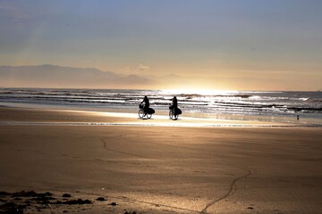 Two girls riding a bicycle on the beach sand at sunset. Lifestyle of friends and couple.