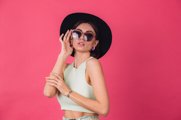 Beautiful stylish woman in hat and sunglasses posing over pink red background, isolated copy space