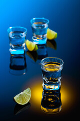Tequila with lime slices on a black reflective background.