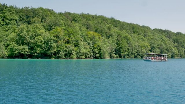 Boat navigating Kozjak Lake in Plitvice as seen from another boat, on a bright, sunny day, with perfect sailing weather. National Park in Croatia, UNESCO world heritage