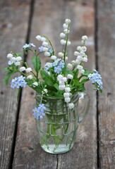 Bouquet of may flowers in a glass on a rustic wooden floor.