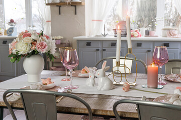 Side view of a dreamy table decor with glasses flowers and lit candles. Wedding easter birthday holiday table setup in a kitchen