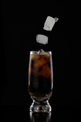 Glass of cola drink with ice cubes falling in it isolated over black background in a studio shot