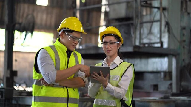 asian industrial Engineer manager man wearing eyeglass and helmet   discussion with mechanic worker woman while using digital tablet checking industry manufacturing large factory . inspection