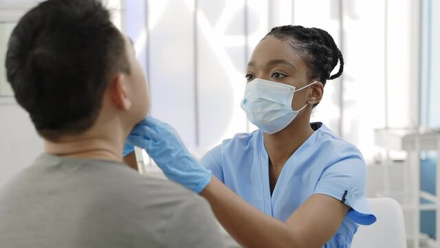 Crop view of medical female nurse in protective mask and gloves taking swab from nose of man in hospital. Concept of PCR diagnostic method, rapid covid test.