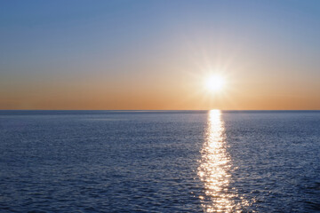 A sunny sunset on the sea stretching into the horizon with a path and highlights on the sea.