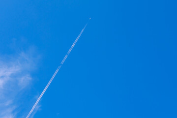 Small white plane with white smoke trail on the blue sky.
