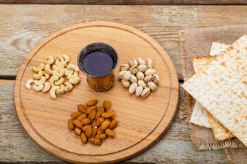 Matzah on a napkin and a round board with nuts and a glass of wine for kiddush on a wooden table.
