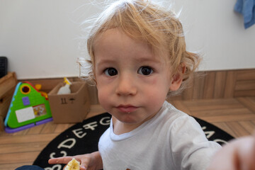 CRIANÇA LOIRA DE UM ANO E 4 MESES OLHANDO PARA A FOTO.