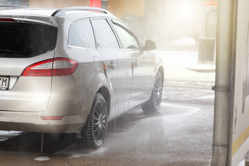 Rear view of a silver car being washed with water and soap in carwash